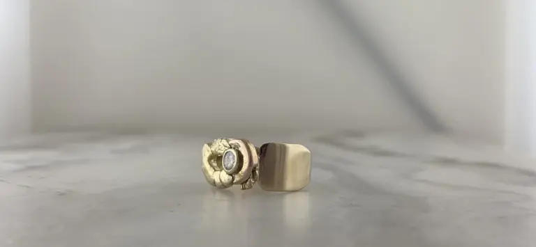 Close-up of two rings, one with a floral design and gemstone, the other plain, placed on a plain surface.