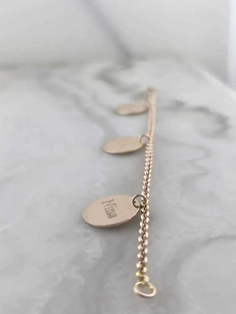 A gold chain bracelet with oval charms, one engraved with the word 'Dream' in cursive, placed on a light gray surface.