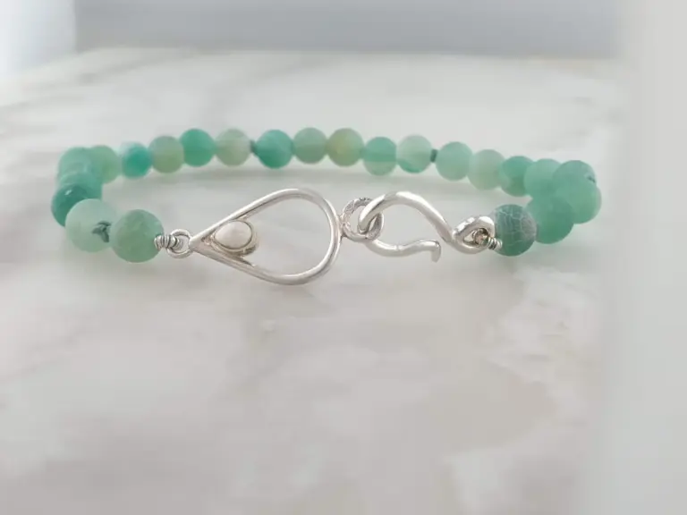 A beaded bracelet with green and blue beads and a silver clasp on a white surface.