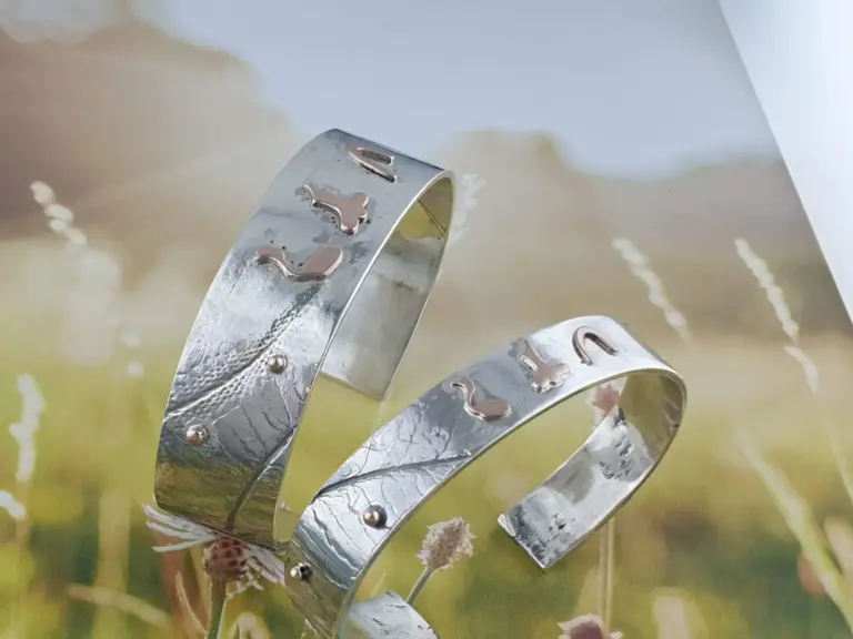 Close-up of three shiny silver rings stacked on a surface with a floral pattern and soft lighting.