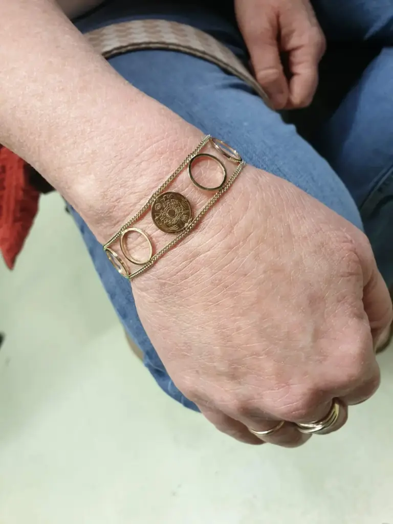Close-up of a person's wrist wearing multiple gold bracelets, including one with a coin charm, and gold rings on their fingers.