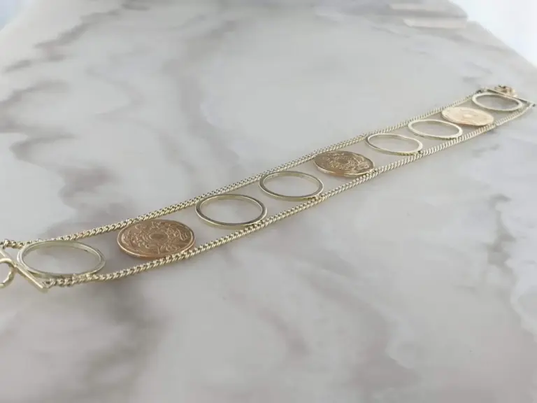 Close-up of layered gold and silver jewelry with hollow oval shapes and coins on a white surface.