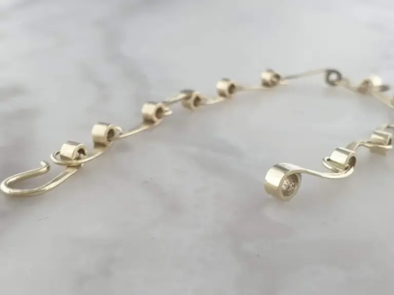 Close-up of a gold chain necklace with cylindrical links resting on a light gray surface.