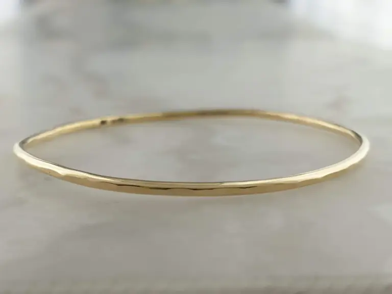 A thin gold bracelet resting on a gray surface.
