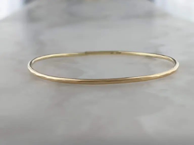 A simple gold wedding band ring on a light-colored surface.