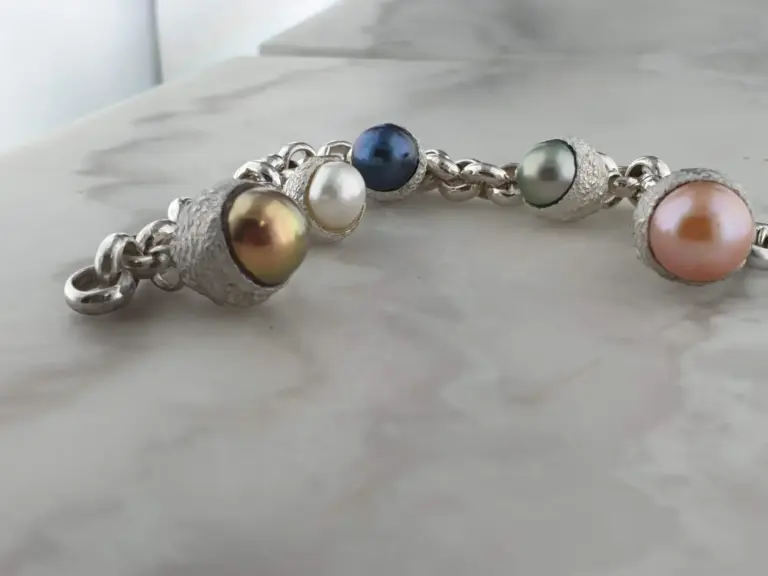 Close-up of a silver bracelet adorned with large multicolored pearls, resting on a white surface.