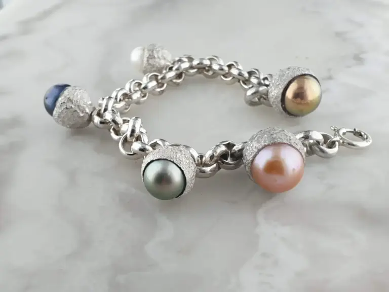 Close-up of a silver chain bracelet with colorful pearl-like beads and textured silver caps on a white surface.