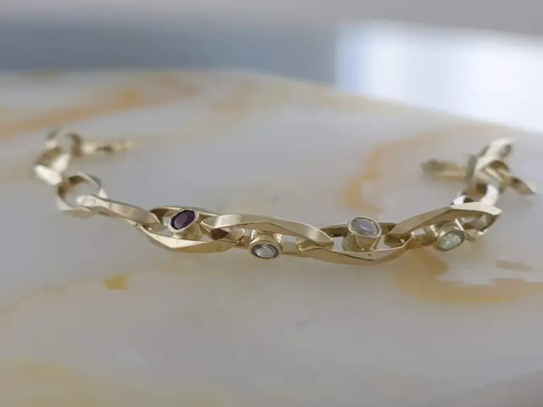 A gold bracelet with gemstone accents resting on a reflective white surface.