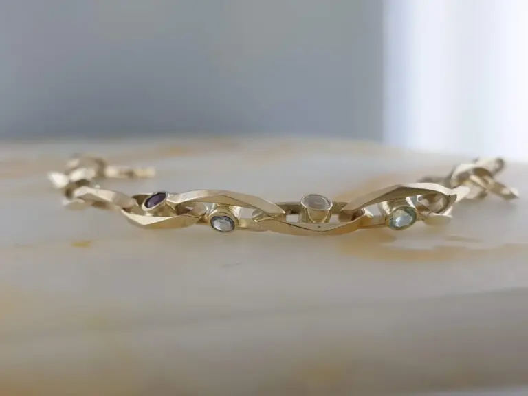 Gold bracelet with oval-shaped gemstones, resting on a white surface.