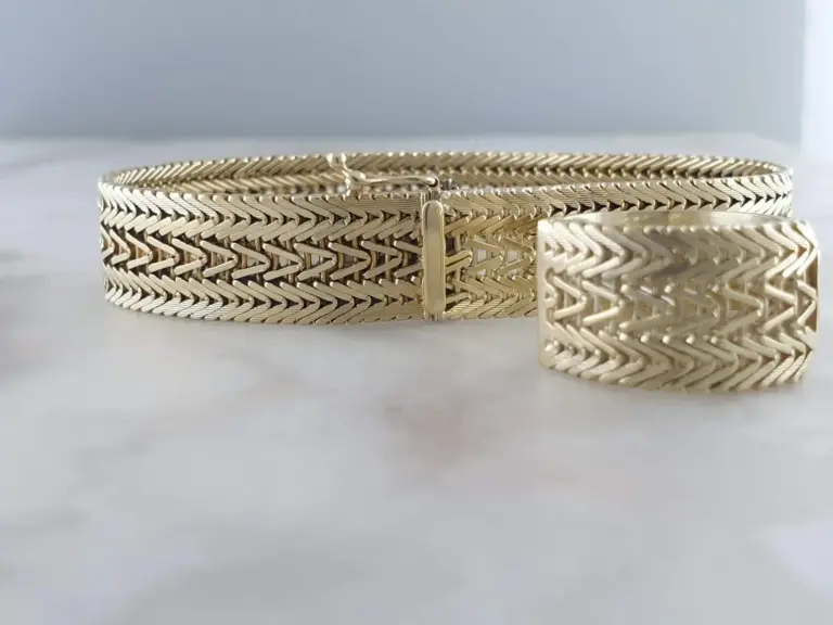 Silver jewelry, including a bracelet and a ring, with intricate woven and herringbone patterns, placed on a white surface.