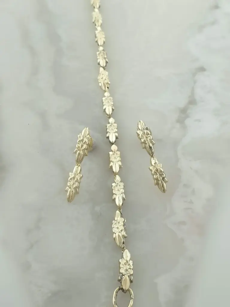 Silver jewelry necklace with floral and leaf designs, laid out on a gray surface.