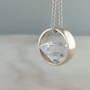 A silver necklace with a round pendant featuring a large, clear gemstone
