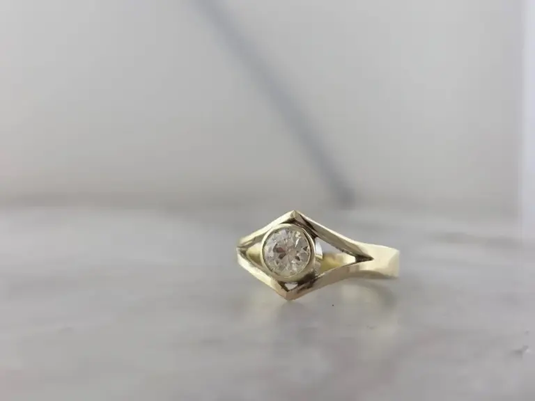 A gold ring with a round diamond in the center, set against a plain, light background.