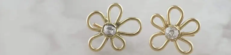 Gold flower-shaped earrings with a central clear gemstone, set against a white background.