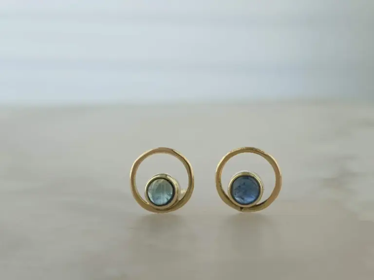 A close-up of four gold rings with blue gemstones, arranged in a row on a light surface.