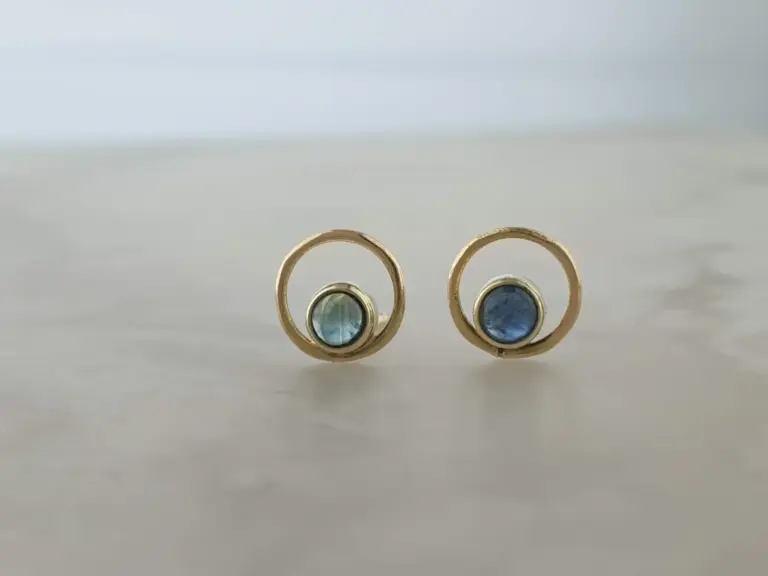 Pair of gold earrings with blue gemstones placed on a white surface with a blurred background.