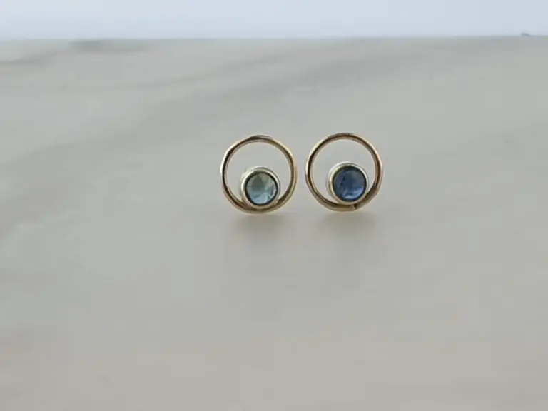 Pair of gold earrings with round blue gemstones on a white surface.