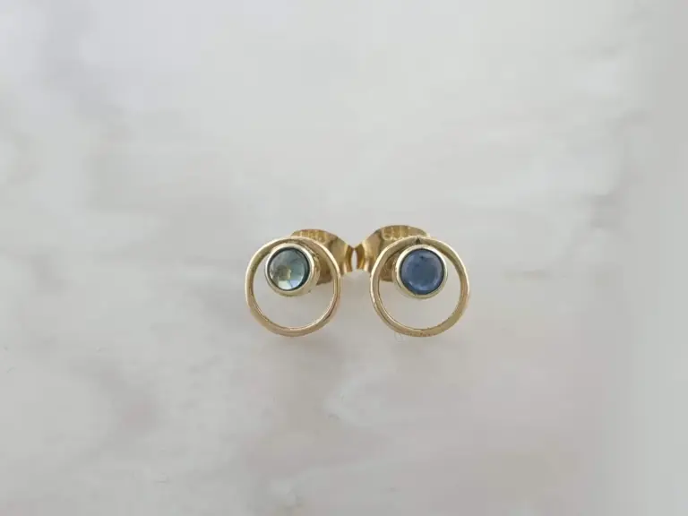 A pair of gold earrings with blue gemstone centers resting on a white surface.