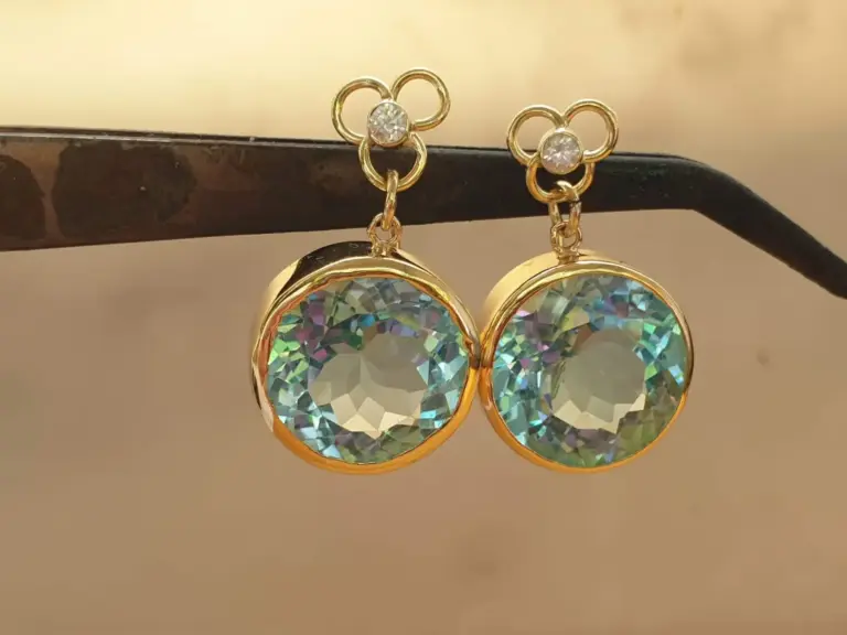 Close-up of gold earrings with shimmering multifaceted heart-shaped stones hanging from a black surface.