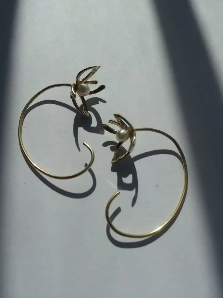Gold earrings with pearl accents on a white surface, casting shadows.