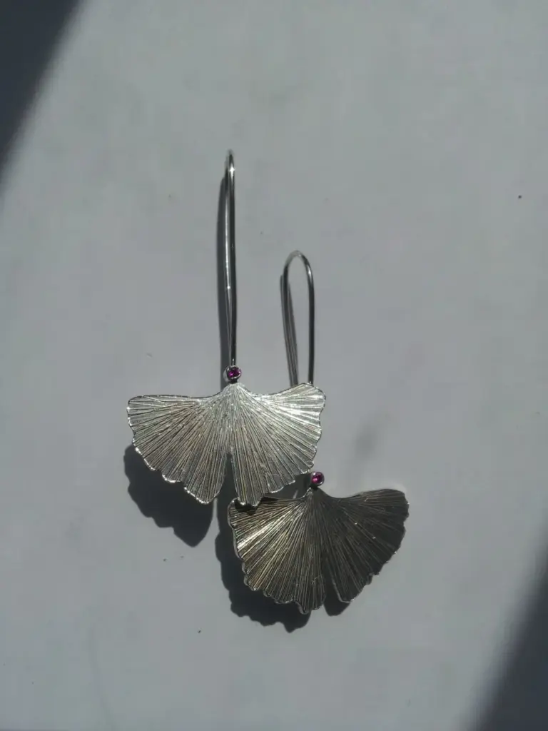 Silver butterfly-shaped earrings with fan-like wings and small purple beads, casting a shadow on a light gray background.