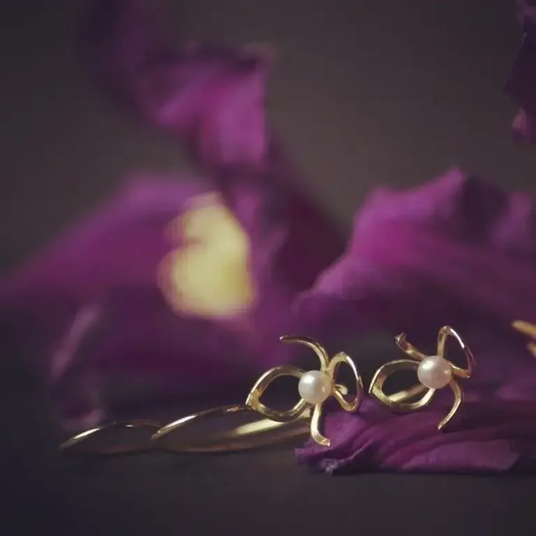 Gold jewelry with pearl accents resting on purple flower petals.