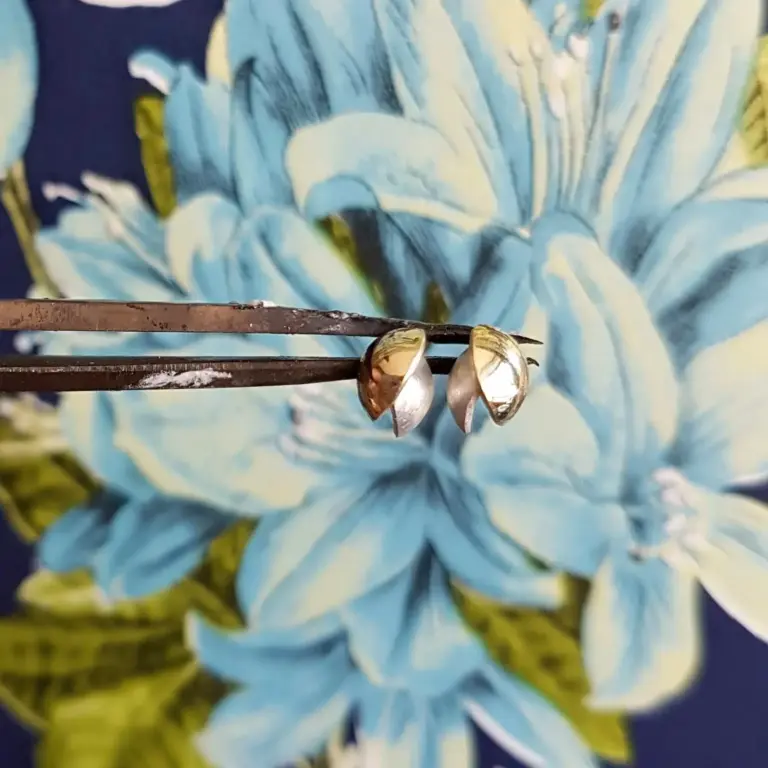 Close-up of small seashells on a dark and yellowish background, with a blurred painting or fabric featuring blue and white hues in the background.
