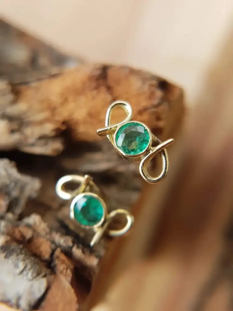 Close-up of a gold ring with a large green gemstone, placed on a piece of bark or wood.