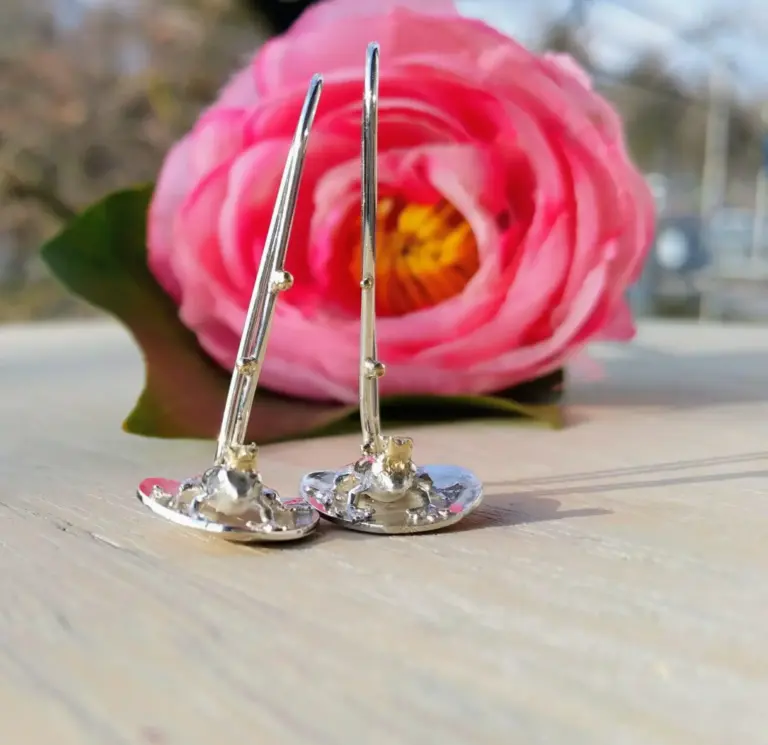 Close-up of a pink rose with metallic jewelry pieces in the foreground.