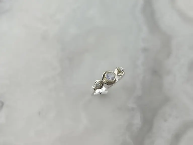 A silver ring with multiple small and large clear gemstones set in a decorative design on a gray surface.