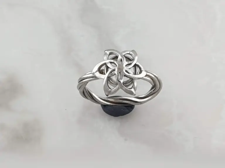 Silver ring with a floral design, resting on a black stand against a plain white background.