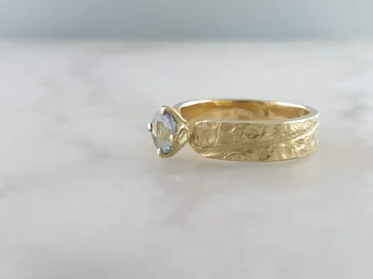 Close-up of a gold ring with a clear gemstone, set against a white background.