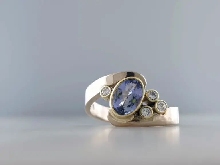 Close-up of a silver ring with multiple clear and blue gemstones set in a floral design, against a plain gray background.