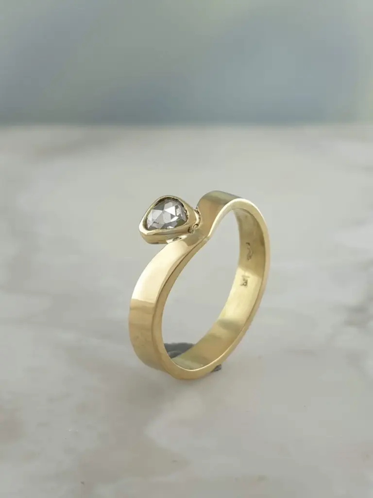 Gold ring with a round, clear gemstone, possibly a diamond, on a plain surface.