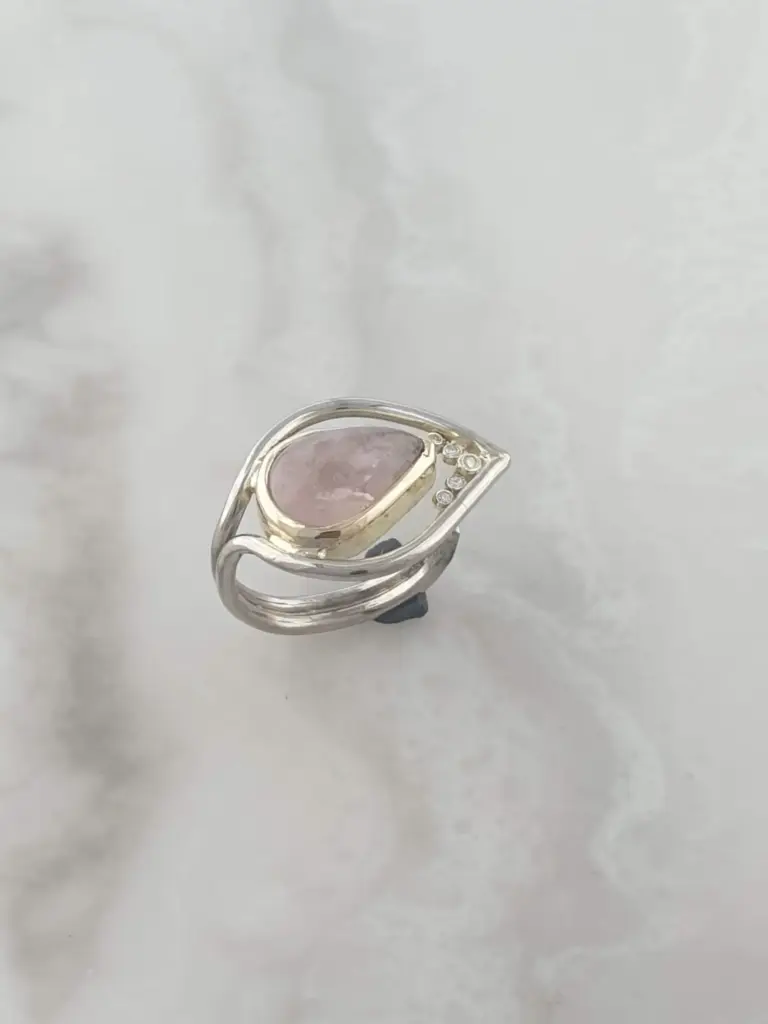 Silver ring with a pink gemstone and small clear stones on a white surface.
