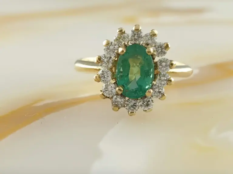 Close-up of a gold ring with a large oval green gemstone and surrounded by small clear diamonds in a floral arrangement.