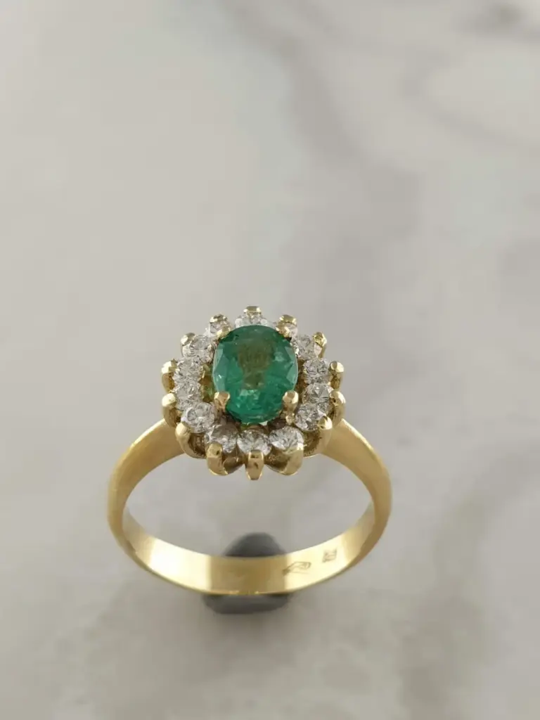 Gold ring with an oval green gemstone surrounded by small diamonds on a white surface.
