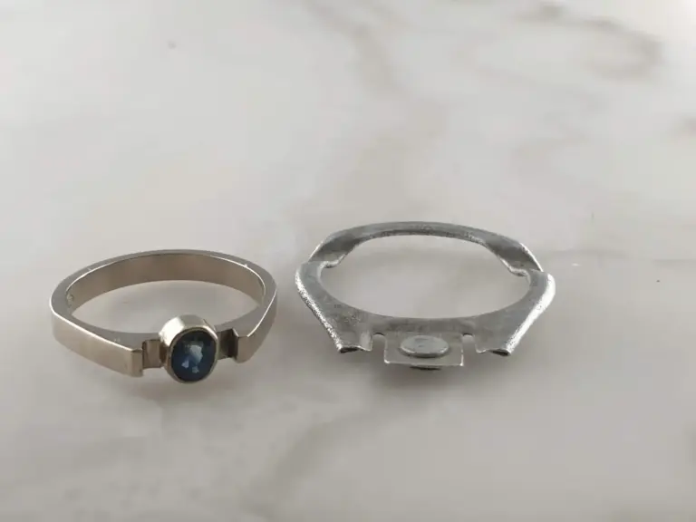 A ring with a blue gemstone and an open silver ring with a decorative design placed on a plain white surface.