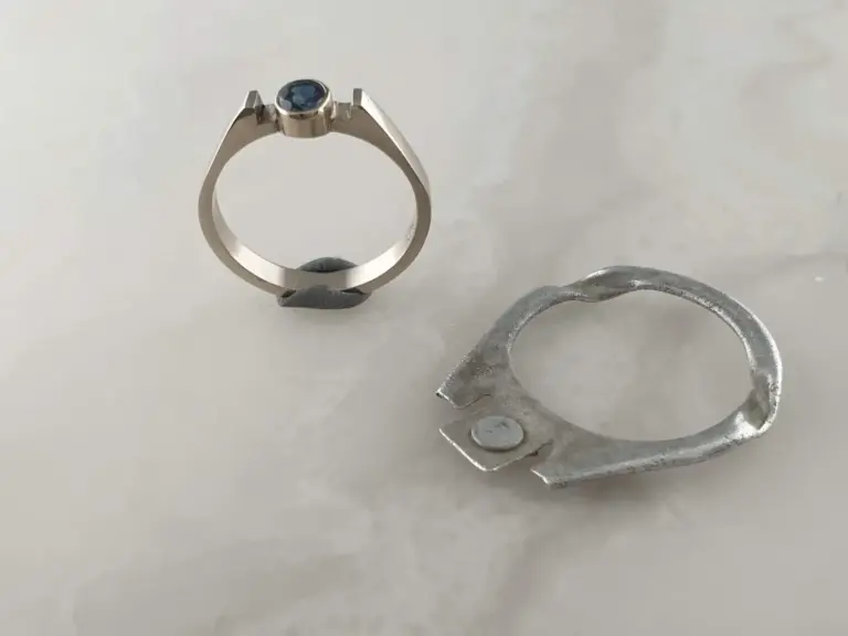 A silver ring with a round blue gemstone in a bezel setting and a silver metal hair clip with a decorative scribble design.