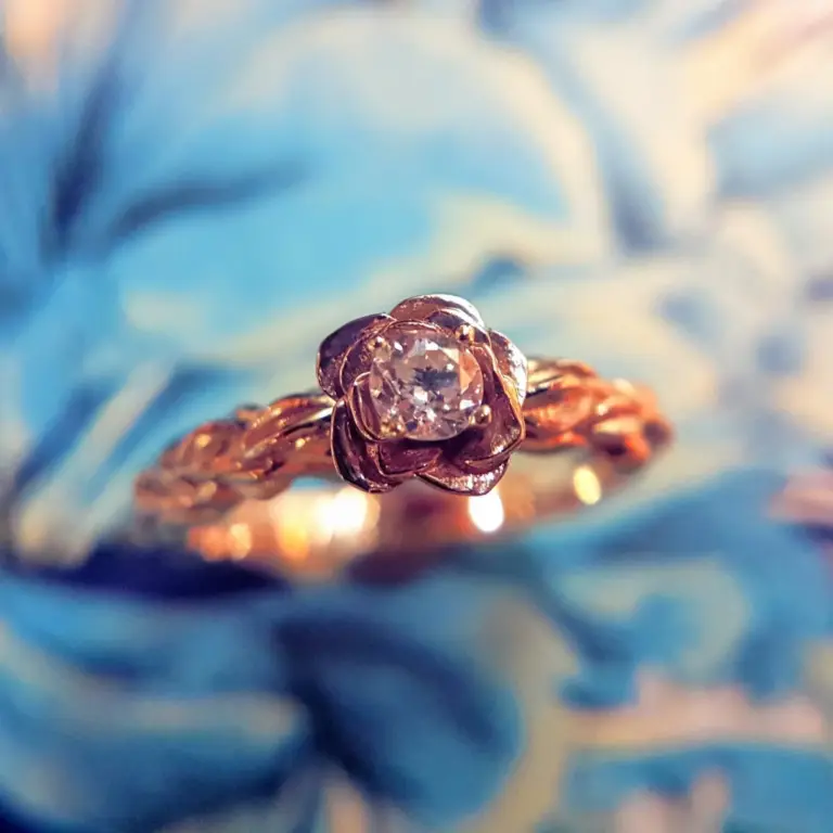 Close-up of sparkling diamond ring on a golden chain against a blurred blue background.