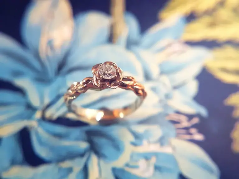 Close-up of a ring with a diamond on a blue flower with yellow accents in the background.