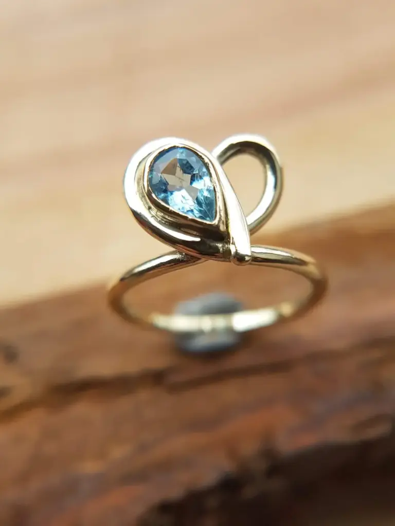 A silver ring with a blue heart-shaped gemstone on a wooden surface.