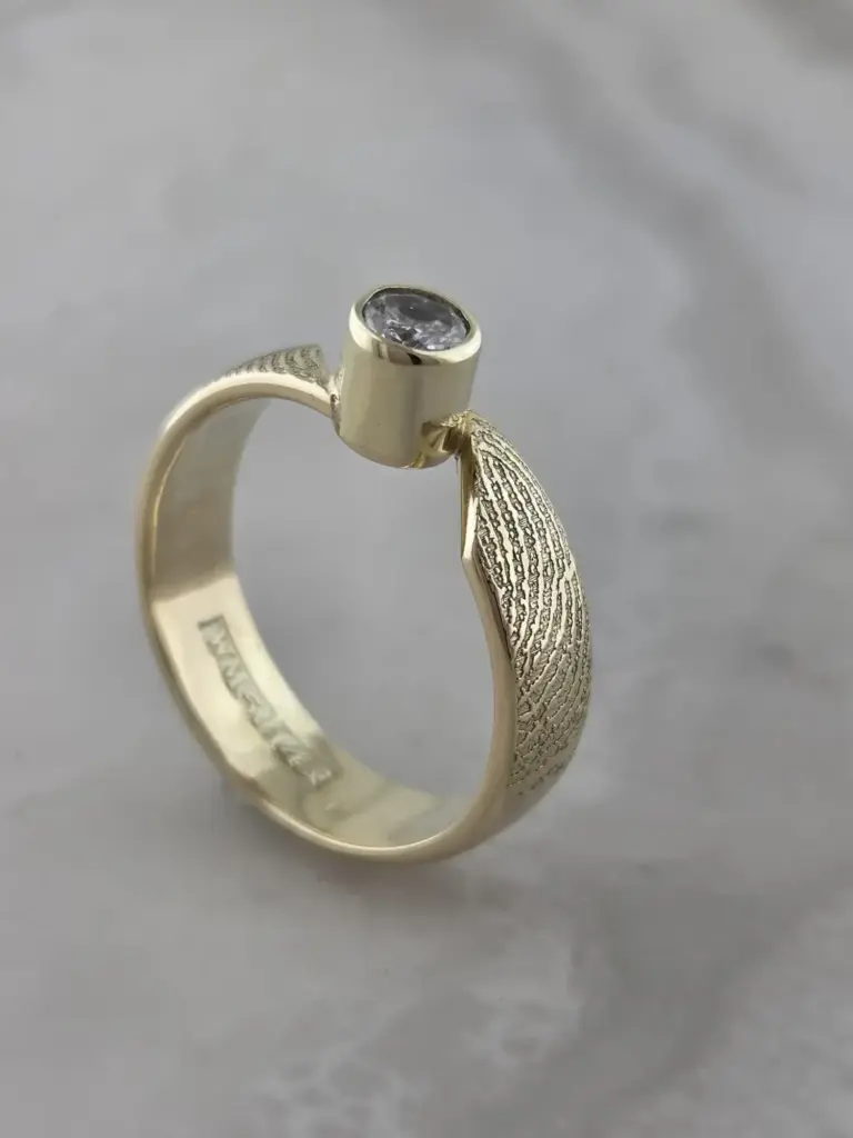 A gold ring with a large clear gemstone and decorative textured gold leaves on the band.