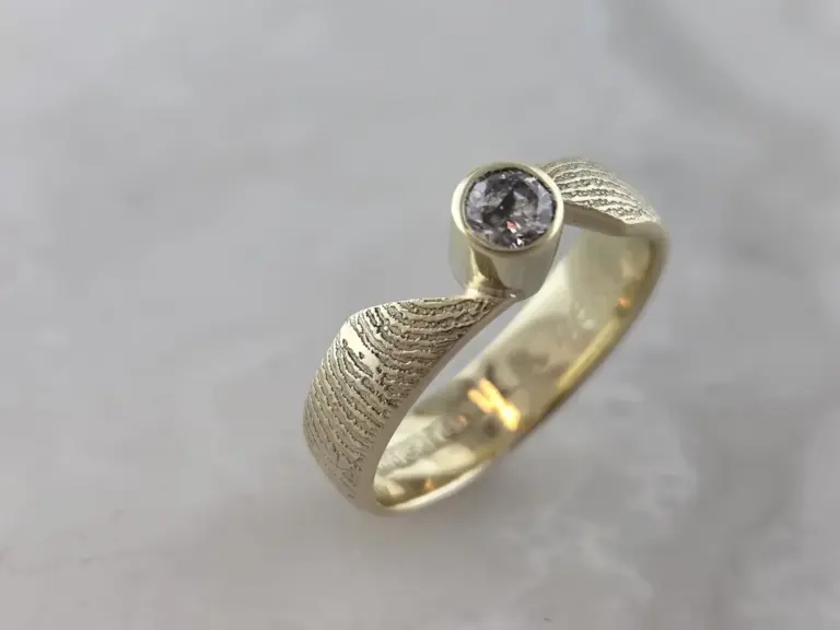 Close-up photo of a gold ring with a central round diamond set in a bezel, with a textured band.