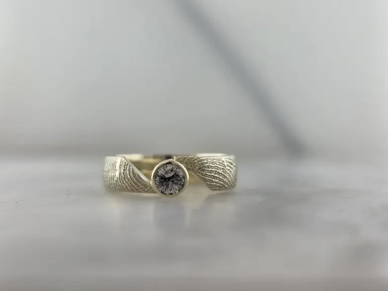 A silver ring with a large round diamond set in the center, placed on a white surface beneath a plain white background.
