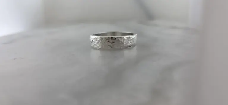 Silver hammered band ring on a plain surface against a plain background.