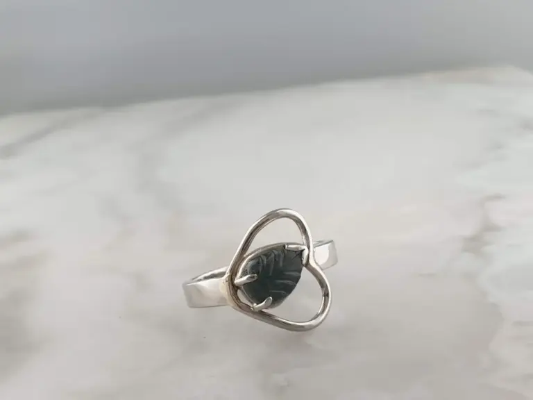 Close-up of a silver ring with a heart-shaped black gemstone on a white surface.