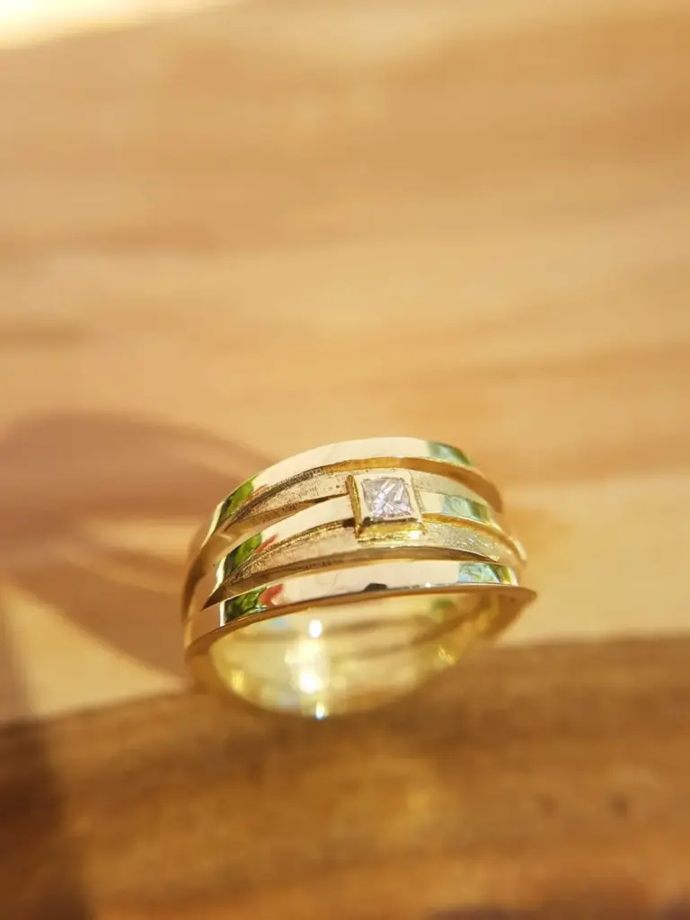 Close-up of gold rings on a wooden surface, with one ring featuring a square diamond.
