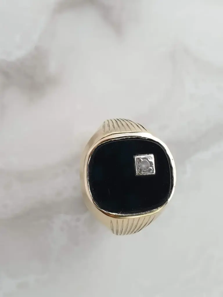 Close-up of a finger with a gold ring featuring a square diamond on a white background.