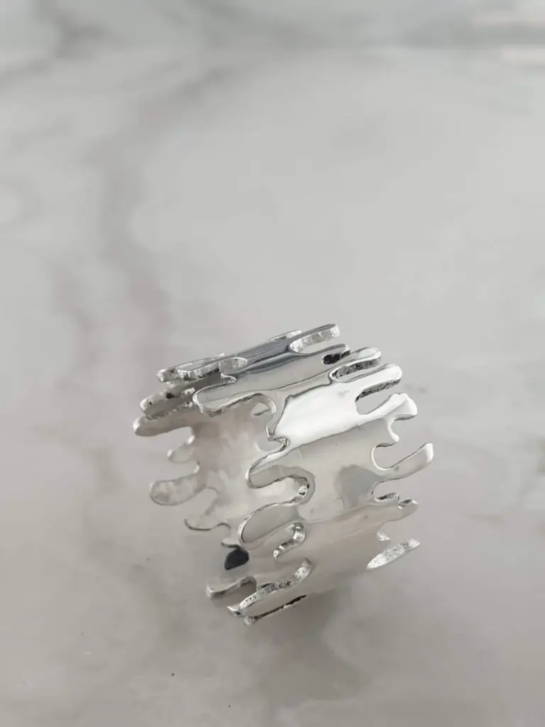 A silver hair clip with a wavy, flame-like design on a plain, reflective surface.